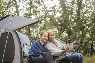 Happy mother taking selfie with daughter on smart phone during tent camping