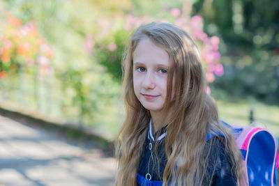 Back to school, portrait of a little girl from primary school outdoors, enjoying flowers 