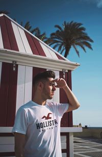 Young man standing by palm tree against sky