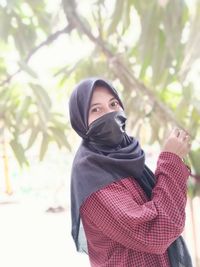 Portrait of young woman standing by tree