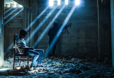 Side view of man sitting on seat in illuminated building