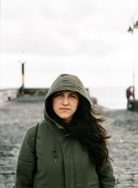 Portrait of woman in warm clothes while standing on pier against sky