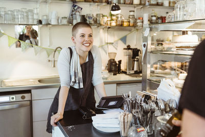 Happy female owner leaning on counter while looking at colleague in cafe