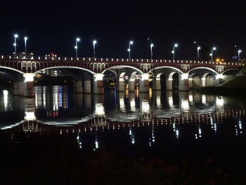 Illuminated bridge over river against sky in city at night