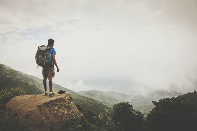 Rear view of man with backpack standing on mountain against sky