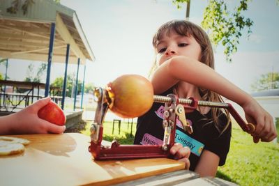 Cute girl holding fruit peeler on table outdoors