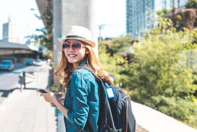 Portrait of smiling young woman standing on mobile phone in city