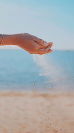 Cropped hands of woman holding sand on shore against sky