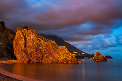 Scenic view of sea by mountain against sky