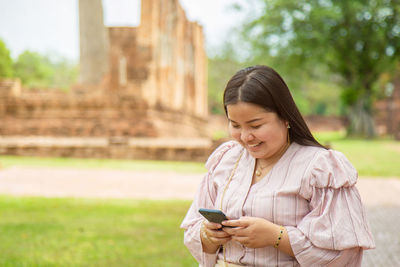 Smiling chubby asian woman using a cell phone while traveling in a buddhist temple in asia.