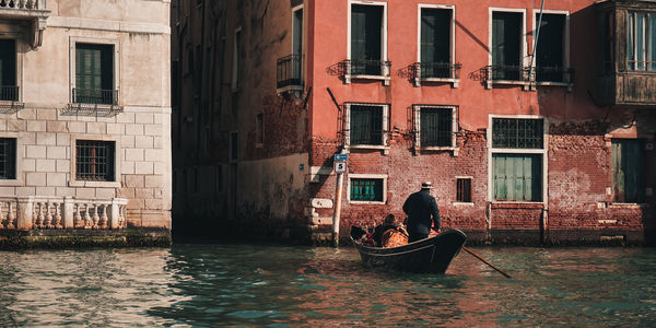 Rear view of man standing in boat on canal against buildings in city