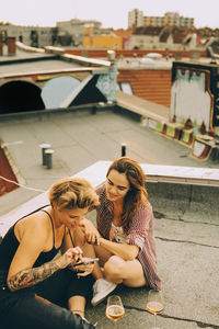 High angle view of friends talking and looking at smart phone while enjoying beer on terrace at party