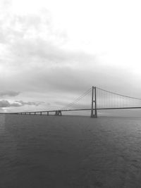 Suspension bridge over sea against cloudy sky