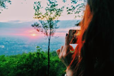 Rear view of woman photographing using phone against sky during sunrise