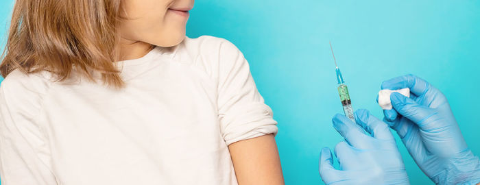 Doctor giving vaccine to girl against blue background