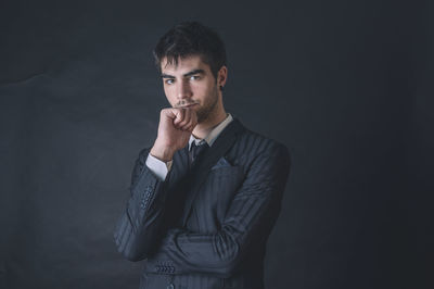 Portrait of young man standing against black background