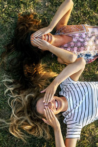 Cheerful young women covering eyes with hands while lying on field
