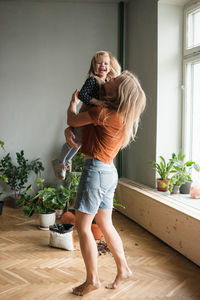 Woman holds in hugs her laughing child in living room with lot plants