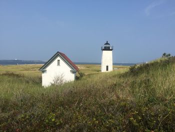 Lighthouse on field by building against sky