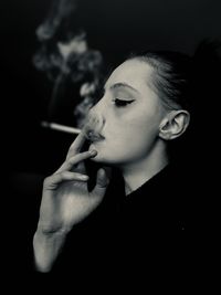 Close-up of young man smoking cigarette against black background