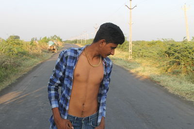 Young man standing on road against trees