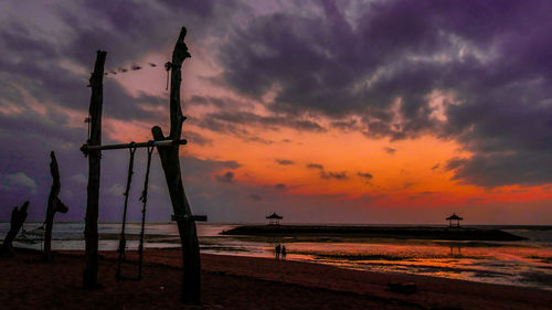 Silhouette cranes on beach against sky during sunset