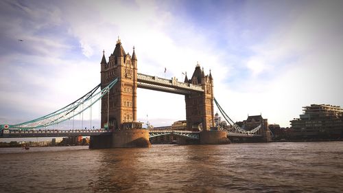 Bridge over thames river against cloudy sky