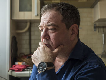 Close-up of thoughtful man with hand on chin looking away at home