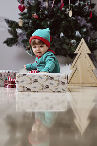 A little 12-month-old christmas elf with a christmas tree and gifts