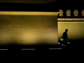 Silhouette man standing against illuminated wall at night