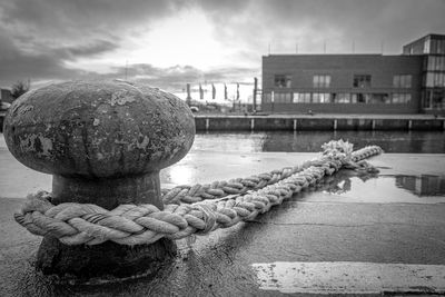 Close-up of rope tied to bollard at harbor against sky