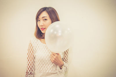 Portrait of young woman holding balloons against wall