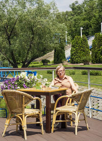 Senior woman drinking while sitting with novel at restaurant