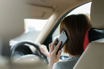 Rear view of woman using smart phone in car