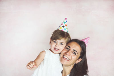 Portrait of smiling mother with cute daughter wearing party hats against wall