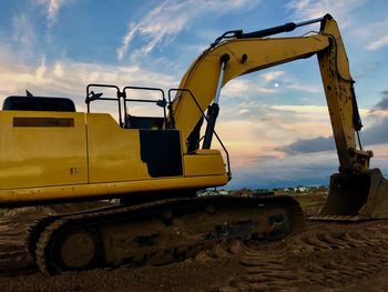 Earth mover at construction site against sky during sunset