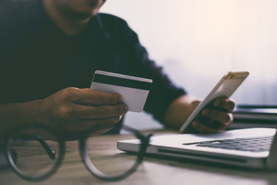 Midsection of man using mobile phone and credit card