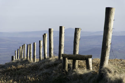 Wooden posts supporting a wire fence near a mountain summit with a stile to aid crossing the fence