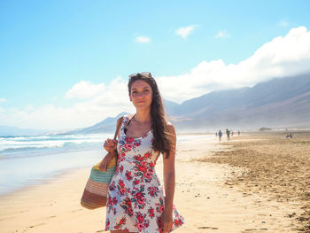 Portrait of woman standing at beach against sky