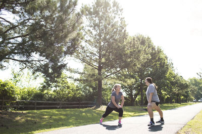 Full length of mother and daughter stretching legs while exercising on footpath at park