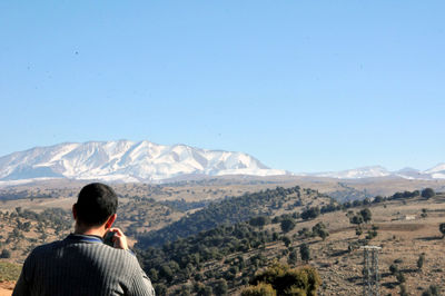 Rear view of man looking at mountains against clear sky