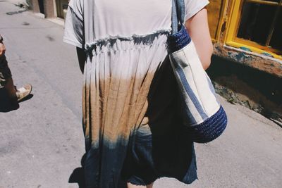 Midsection of woman carrying purse on footpath during sunny day