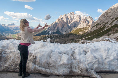 Side view of woman playing with snow on snowcapped mountains against sky