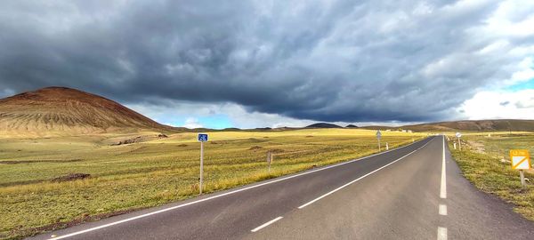 Road amidst field against dramatic sky