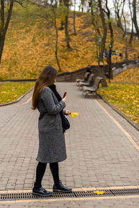 Rear view of woman standing on footpath during autumn