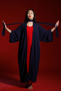 Portrait of young woman wearing graduation gown standing against yellow background