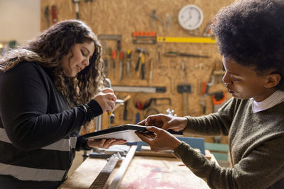 Woman helping technician repairing laptop using tool at recycling center