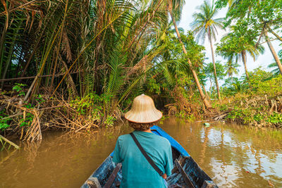 Rear view of man on palm tree by river