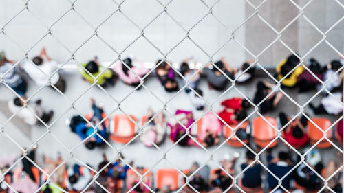 Directly above shot of people sitting on chairs seen through chainlink fence