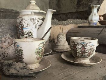 Close-up of old dirty cup and saucer with kettle on table in abandoned building